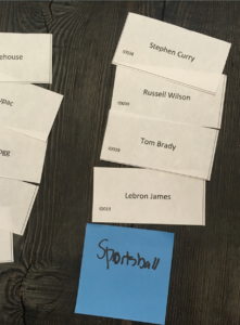 Clusters of notecards and post-it notes on a table. Each note card has the name of a professional athlete. The post-its have handwritten categories.