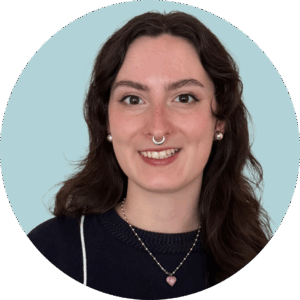 Gigi Shannon Professional portrait of a woman with long, dark hair and a septum ring smiling at the camera against a blue background